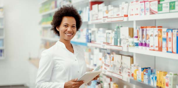 A female pharmacist looks at camera smiling near shelves filled with prescriptions.