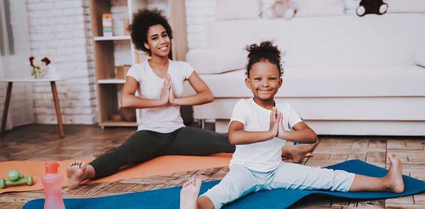 A woman and her young daughter practice yoga on their living room floor.