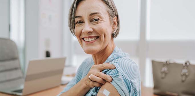 A woman smiles, showing a bandage from a recent vaccination